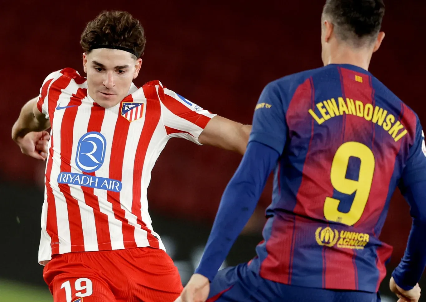 Dwóch piłkarzy walczy o piłkę podczas meczu, jeden w biało-czerwonej koszulce Atlético Madryt, drugi w bordowo-granatowej koszulce FC Barcelona z numerem 9 i nazwiskiem Lewandowski na plecach.