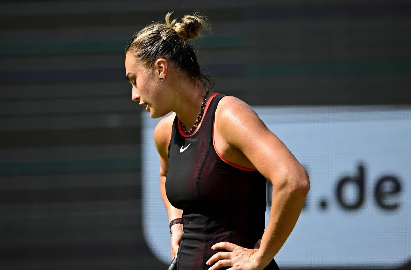 Zmęczona tenisistka w czarnej sportowej sukience i zebranych włosach odpoczywa na korcie podczas meczu.