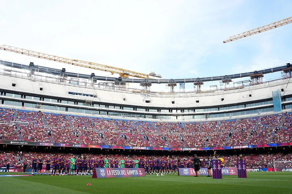 Piłkarze FC Barcelony ustawieni na murawie Camp Nou, w tle trybuny z kibicami i żurawie budowlane.